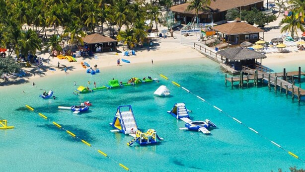 Una playa con agua turquesa cristalina, un muelle y diversas actividades acuáticas.