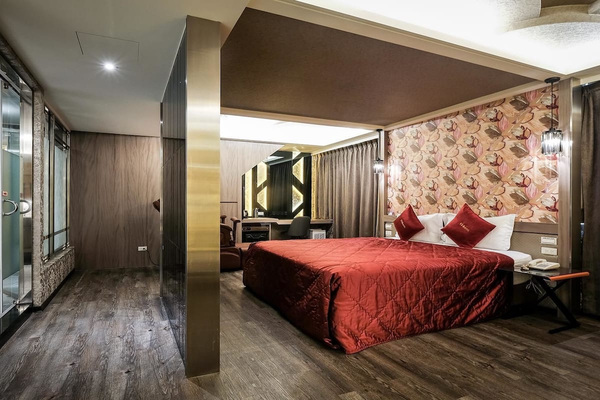 A hotel room with a large bed, a desk with a chair, a mirror, and a shower area.