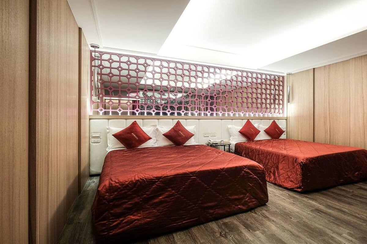 A hotel room with two beds, a wooden floor, and a decorative partition with a geometric pattern.