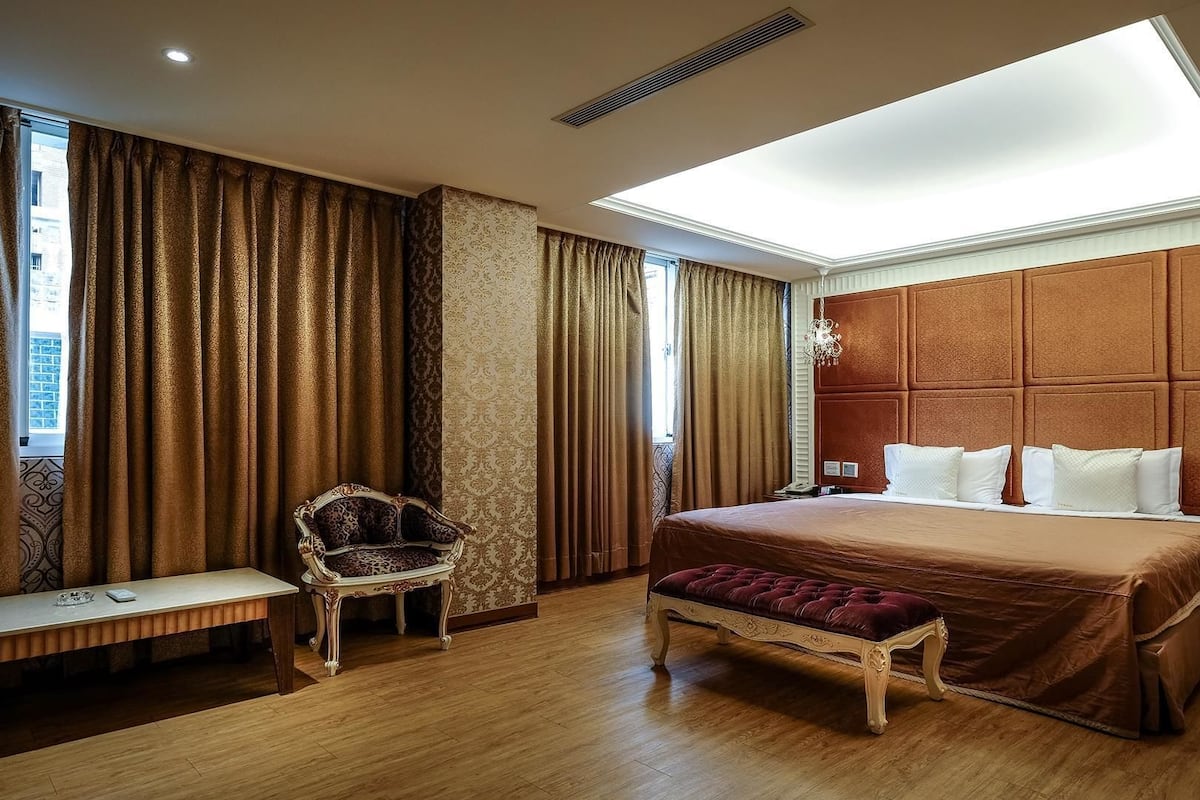 A hotel room with a large bed, a bench, a chair, and a desk.