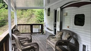 En overdækket veranda med fletningsmøbler og udsigt til en campingvogn.