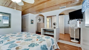 A bedroom with a bed, a dresser, a vanity with a mirror, and a wall-mounted TV.