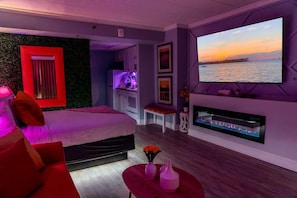 A modern bedroom with a bed, a TV, a fireplace, and a view of the sea.