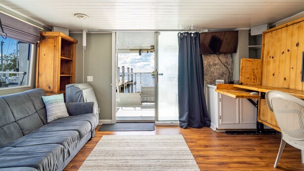 Un intérieur de camping-car moderne avec un canapé gris, des meubles en bois, une table à manger et une grande porte-fenêtre coulissante donnant sur un espace extérieur.