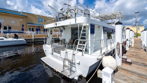 Un bateau blanc était amarré dans une marina, doté d’un pont en bois, de garde-corps en métal et d’un espace de repos abrité.