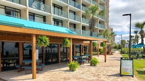 A covered outdoor seating area with tables and chairs, surrounded by a brick walkway, and a signboard advertising a special offer. - Oceanfront Studio Retreat on the Golden Mile (Myrtle Beach)