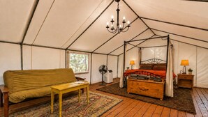Ein Zelt mit Bett, einer Couch, einem Tisch und einem Ventilator.