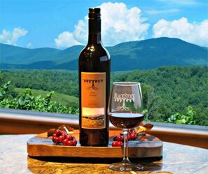 A bottle of wine and a glass on a wooden board with a scenic view of mountains and greenery in the background.