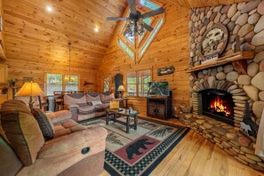 L’intérieur chaleureux d’un chalet en rondins, avec une cheminée en pierre, un plafond en bois et un coin salon confortable.