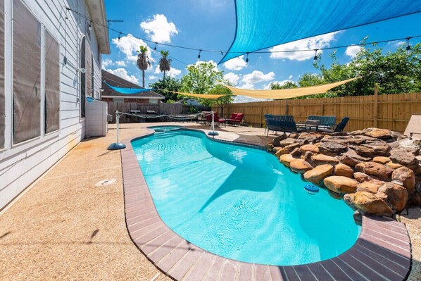 Un patio trasero con piscina, rodeado por una valla de madera, y con una zona de patio amueblada al aire libre.