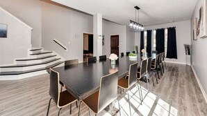 Ein geräumiger Essbereich mit einem langen Tisch, Stühlen, einer Treppe und einer modernen Kronleuchter.