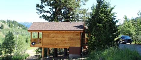 A wooden cabin with a balcony, surrounded by trees and a dirt path.
