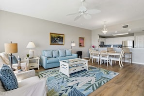 A living room with a sofa, coffee table, and dining area with chairs. - Ocean Park 206 - Hosted By Moore AI Rentals (Fernandina Beach)