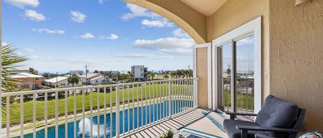 Un balcón con vista a una piscina, una mesa de comedor y una silla.