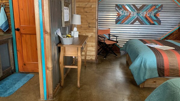 A cozy room with a wooden desk, a chair, a bed with a patterned bedspread, and a wall with a geometric design.