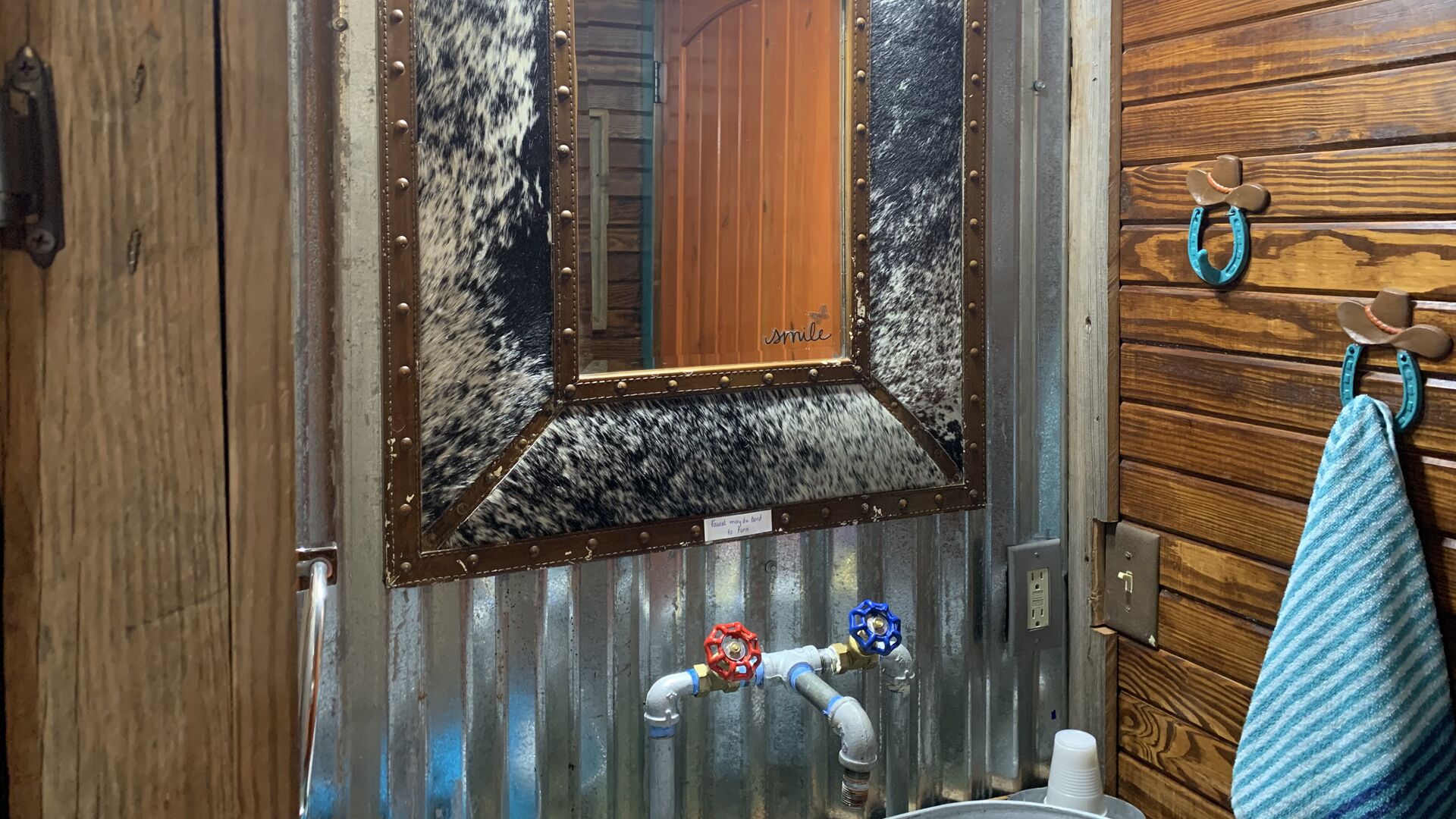 A rustic bathroom with a wooden door, a mirror with a cowhide pattern, and a towel rack with a blue towel.