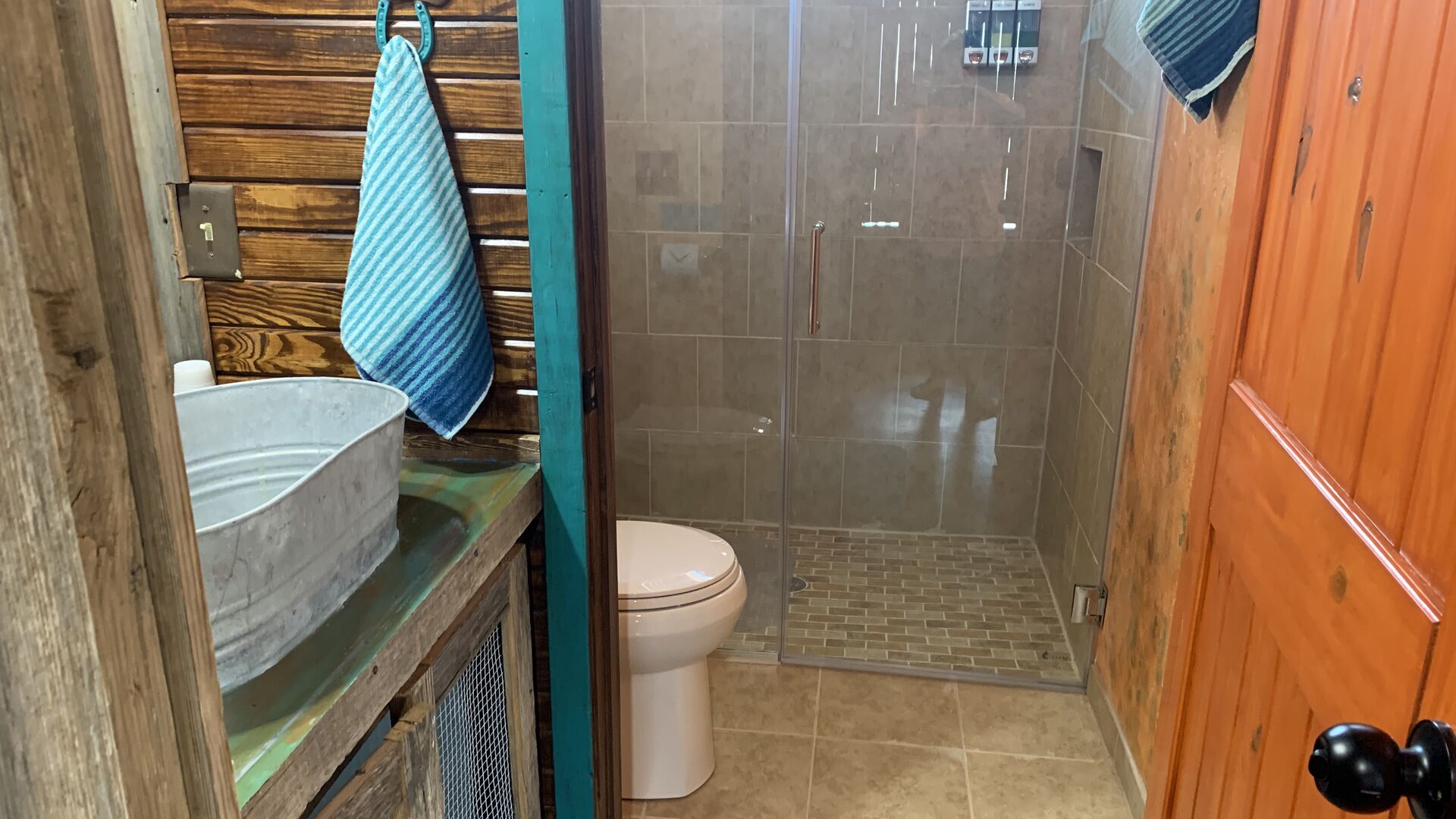 Une salle de bain avec un meuble-lavabo en bois, des toilettes blanches et une cabine de douche en verre.