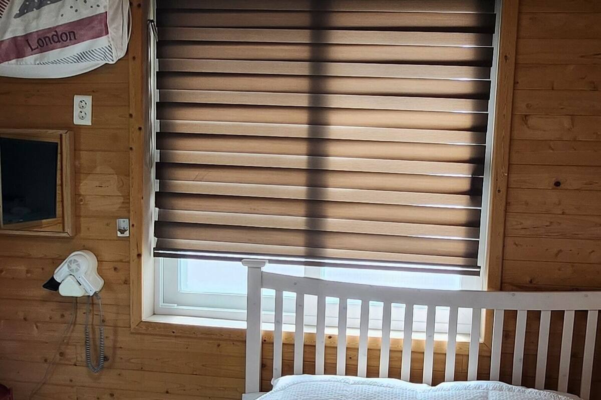 Een slaapkamer met een bed, een raam met zonwering, een plafondventilator en een vlag aan de muur.