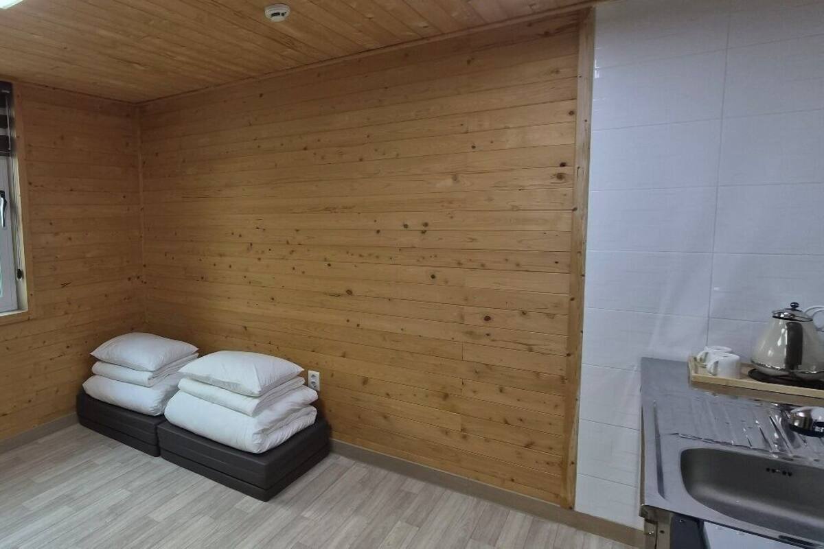 Een kamer met houten lambrisering, een raam, een wastafel en een bed met kussens.