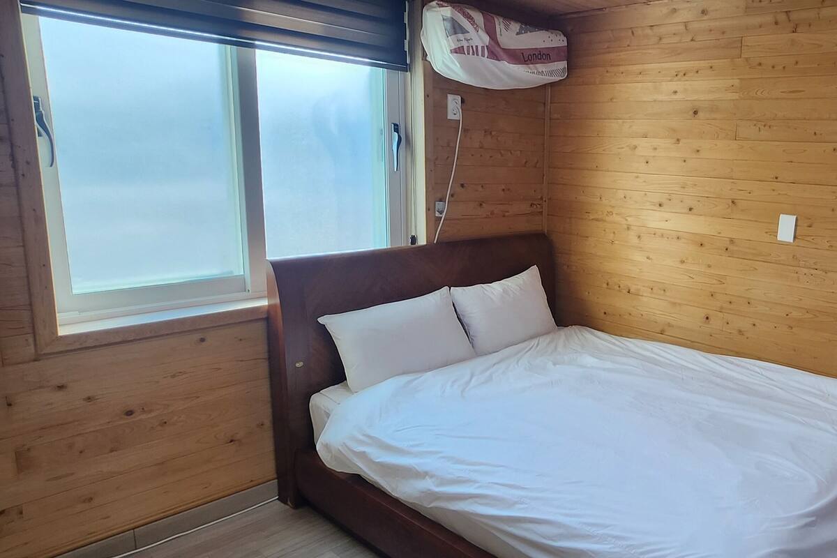 Een kamer met houten lambrisering, een bed, een raam en een wandhaak.