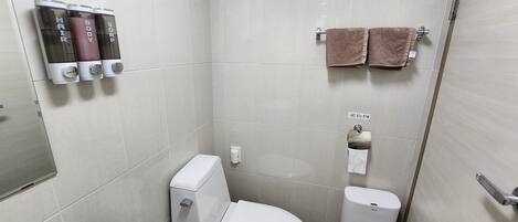 A bathroom with a toilet, a towel rack with two towels, and soap dispensers labeled 'HAIR,' 'BODY,' and 'SOAP.'