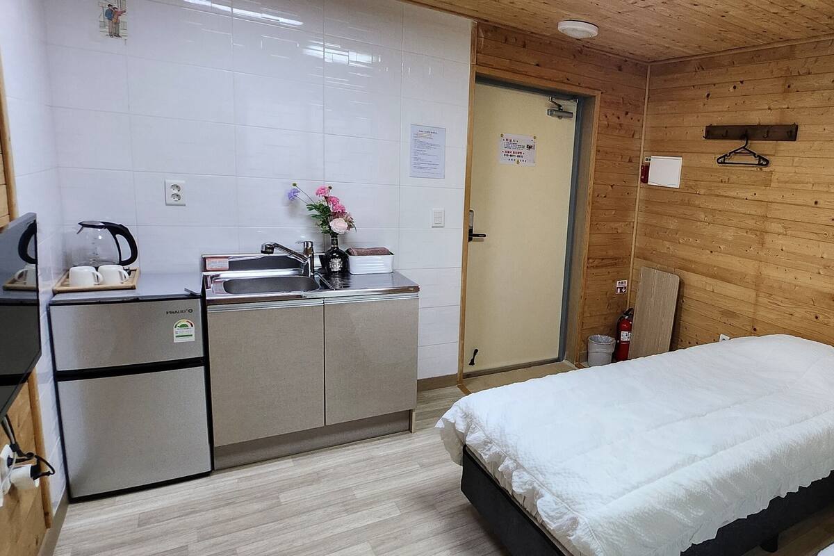 Een knus, compacte kamer met kitchenette, twee bedden en houten wanden.