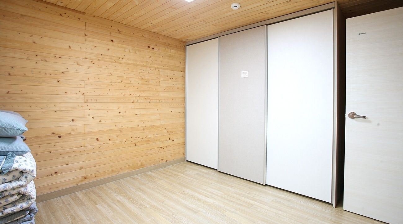 A room with wooden panel walls, a bed with a blue and white duvet, and a white wardrobe with a sliding door.