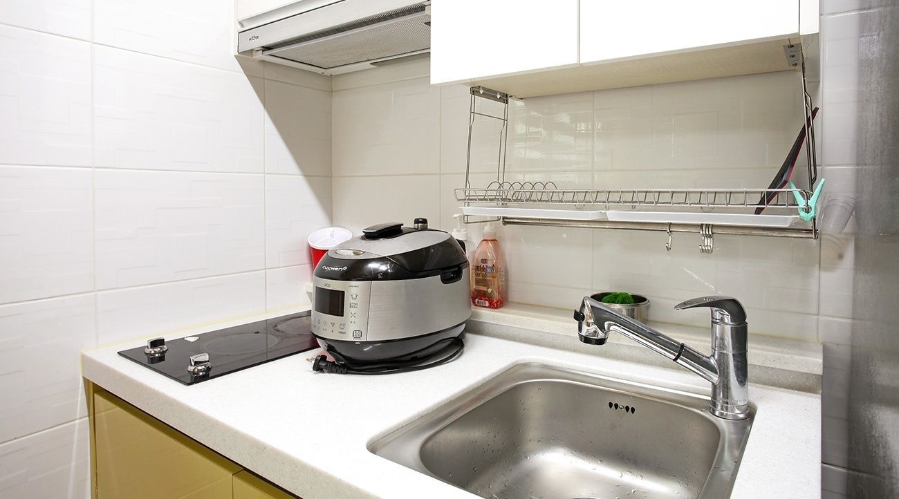 A kitchen with a built-in rice cooker, a stainless steel sink, and a drying rack above the sink.