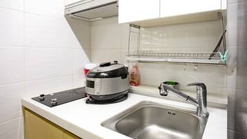 A kitchen with a built-in rice cooker, a stainless steel sink, and a drying rack above the sink.