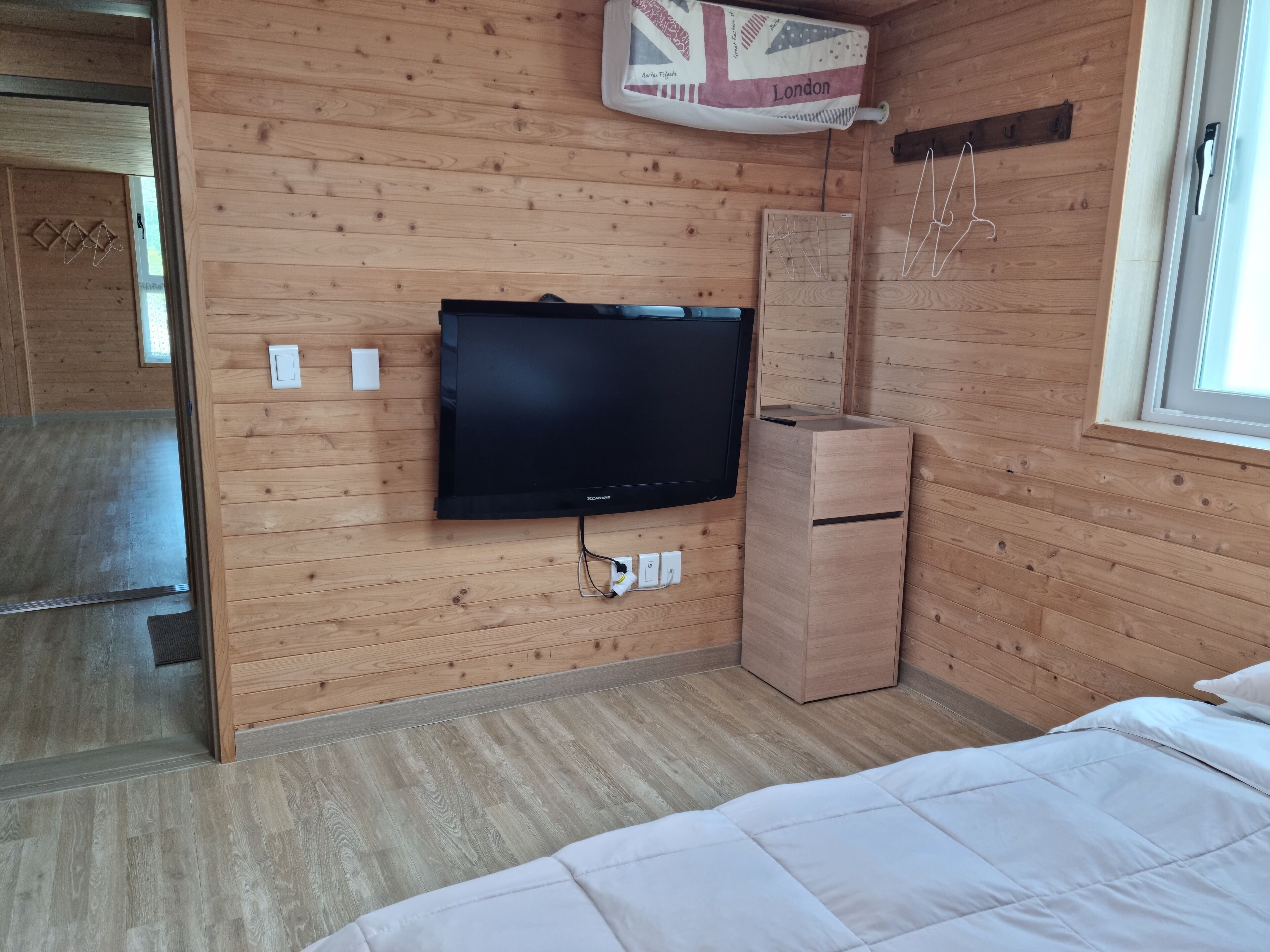 A wooden-paneled room with a flat-screen TV mounted on the wall, a wooden cabinet, and a bed with white bedding.