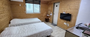 Een houten kamer met twee bedden, een televisie, een wastafel en een raam.
