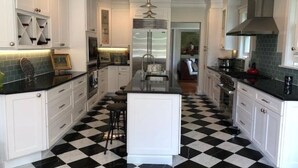 A kitchen with white cabinetry, a black and white checkered floor, a central island, and a stainless steel range hood.