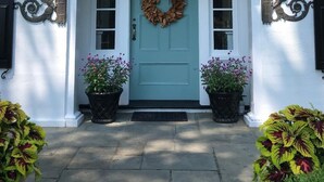 A front entrance with a teal door, a wreath, and two potted plants with flowers.