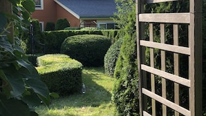 A garden with a wooden gate, neatly trimmed hedges, and a house in the background. - Cripple Cove Apartment in historic home across from harbour in Gloucester, MA (Gloucester)