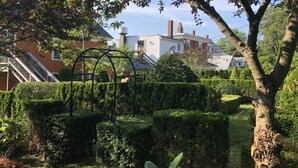 A residential area with a well-maintained garden, a metal arch structure, and houses with visible chimneys. - Cripple Cove Apartment in historic home across from harbour in Gloucester, MA (Gloucester)