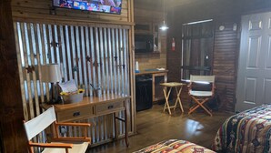 A cozy room with a wooden desk, a chair, a bed, and a television mounted on the wall. - Chief Cabin at The Lazy Buffalo Explore the Wichita Mountains Relax & Unwind (Cache)