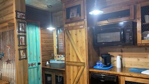 A rustic kitchen with wooden walls, a turquoise door, a microwave, and a dishwasher. - Chief Cabin at The Lazy Buffalo Explore the Wichita Mountains Relax & Unwind (Cache)
