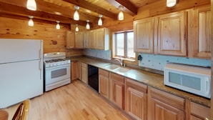 A kitchen with wooden cabinets, a stove, a sink, and a microwave. - Enjoy a private mountain retreat at Paul's Cabin! (Hartsel)