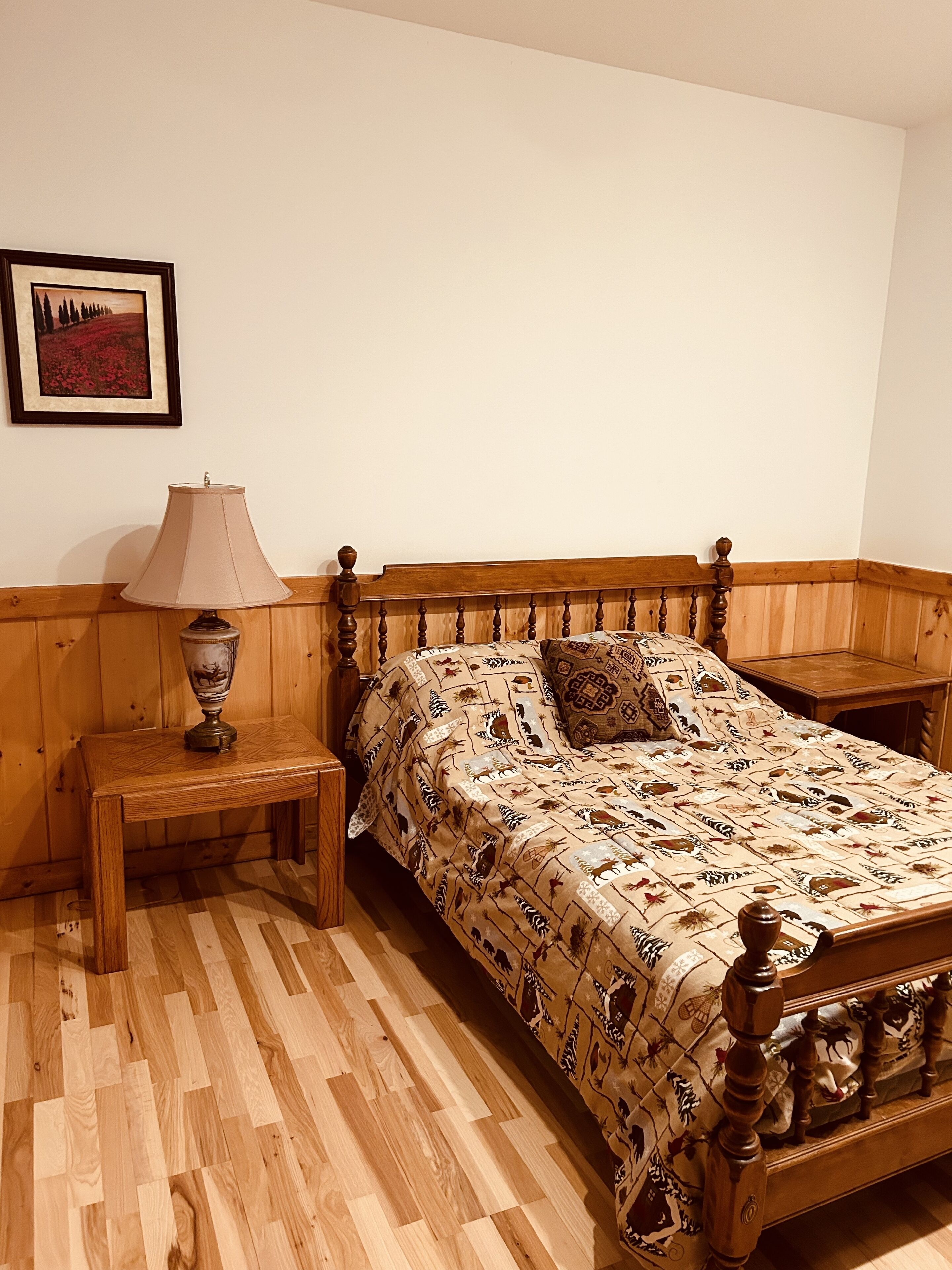 A bedroom with a wooden bed, a nightstand, a lamp, and a framed picture on the wall.