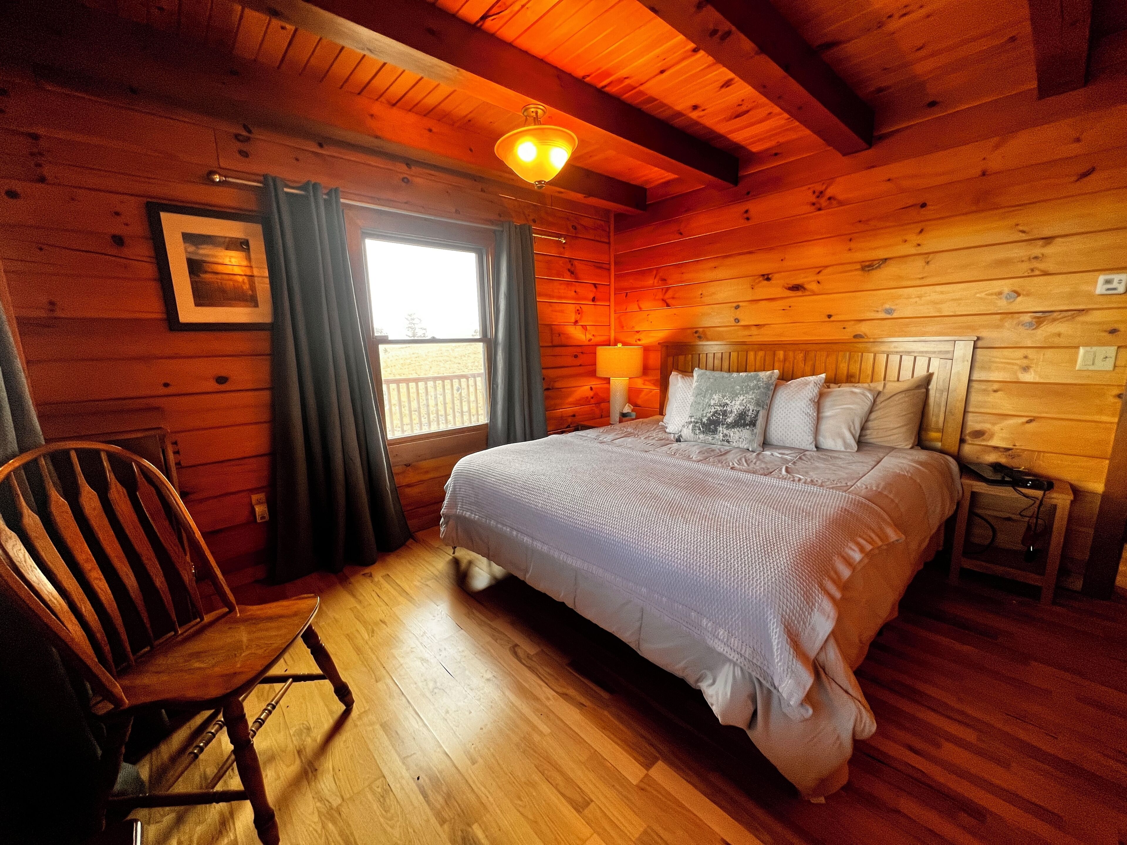 Une chambre dans une cabane en bois, avec un lit, une chaise, une fenêtre avec des rideaux et un plafond en bois.