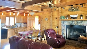 A wooden cabin interior with a dining area, leather chairs, a fireplace, and a kitchen in the background. - Enjoy a private mountain retreat at Paul's Cabin! (Hartsel)