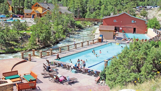 A resort with a swimming pool, lounge chairs, and a view of a river and forested hills. - Enjoy a private mountain retreat at Paul's Cabin! (Hartsel)