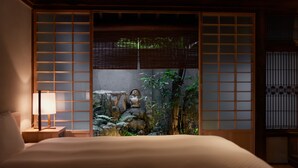A traditional Japanese-style room with tatami flooring, a low wooden bed, a shoji screen, and a small indoor garden with rocks and plants.