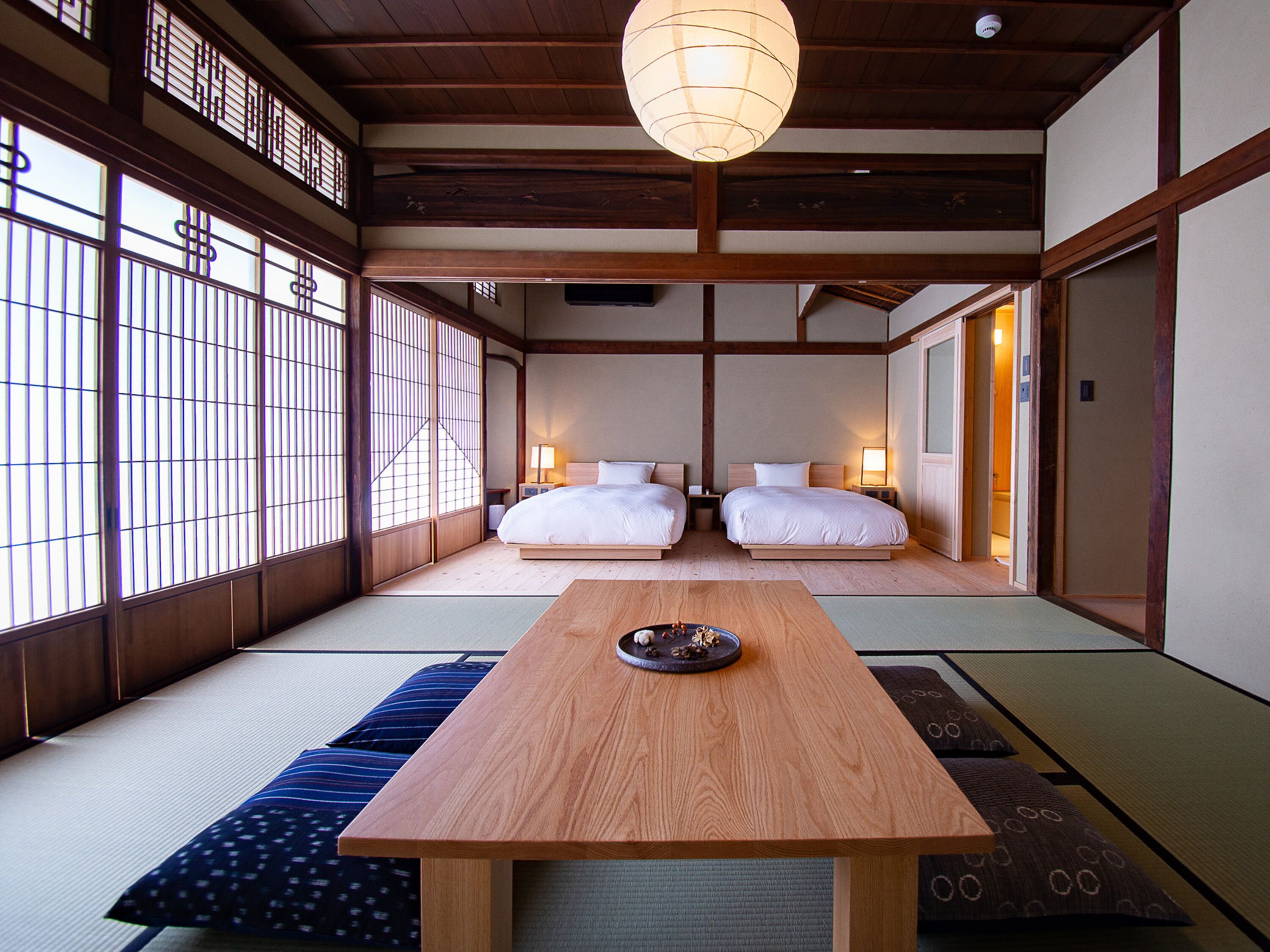 Una habitación de estilo japonés tradicional con suelo de tatami, dos camas, una mesa de madera y puertas correderas.