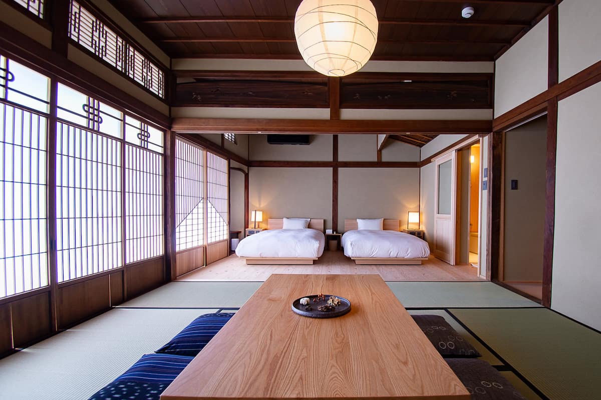 Una habitación de estilo japonés tradicional con suelo de tatami, dos camas, una mesa de madera y puertas correderas.