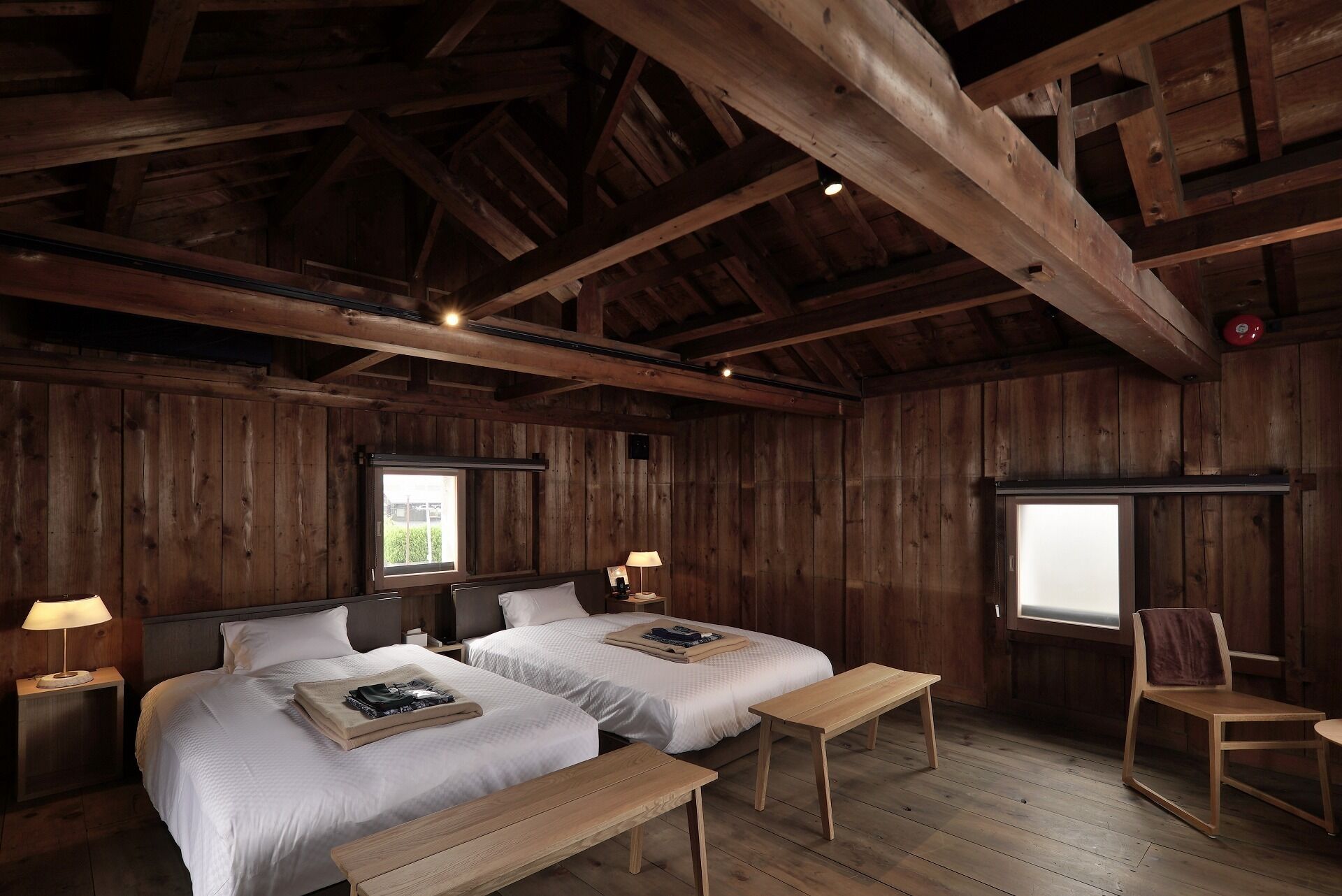 A rustic wooden room with two beds, a bench, and a chair.