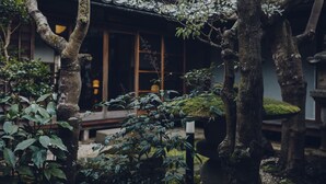 A traditional Japanese building with a tiled roof, surrounded by mature trees and lush greenery.