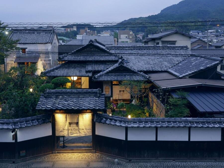 Un edificio japonés tradicional con techo de tejas, entrada central y un cartel que indica que es un hotel.