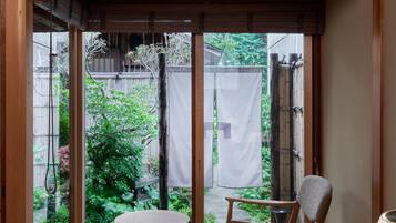 Una habitación japonesa tradicional con suelo de tatami, una mesa de madera baja, una silla y un puertas correderas que dan a un jardín.