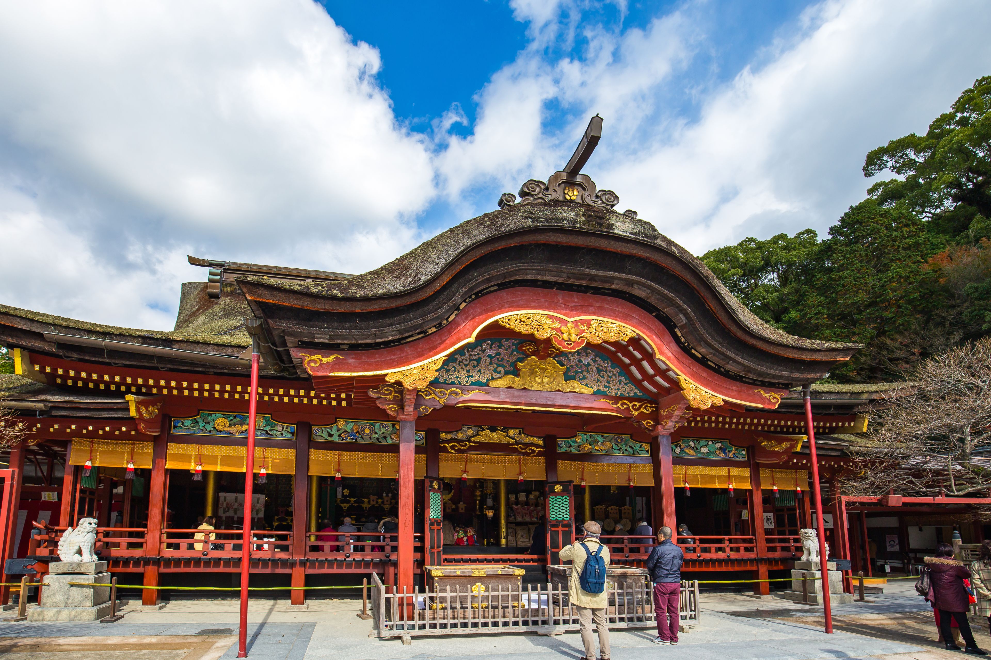 A traditional building with a red and gold roof, a stone lion statue in front, and a clear blue sky.